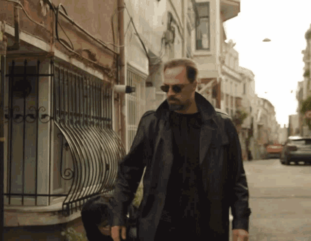 a man wearing sunglasses and a black leather coat walks down a street