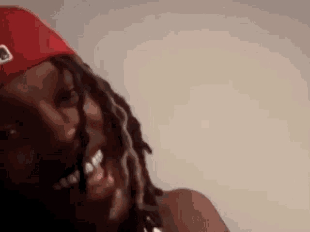 a close up of a person with dreadlocks wearing a red hat and smiling .