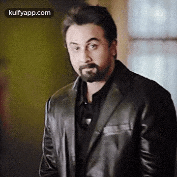a man with a beard is wearing a black suit and a leather jacket .
