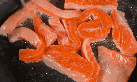 slices of salmon are being cooked in a skillet