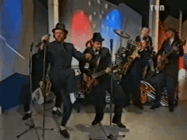 a group of men are playing instruments in front of a tv screen
