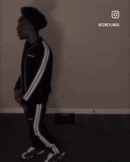 a man in a black and white tracksuit is standing in a room .