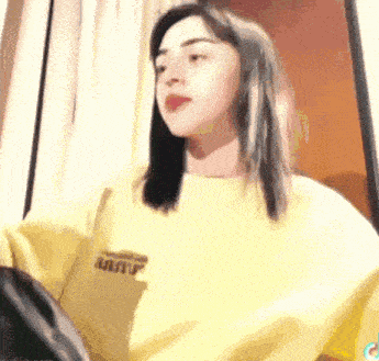 a woman is wearing a yellow sweater and looking out a window .