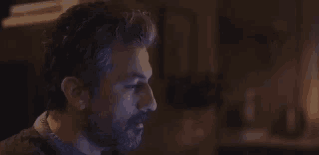 a man with a beard is sitting in a dark room looking at a computer screen .