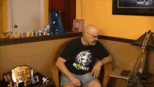 a man wearing a black shirt that says rarity sits in a chair