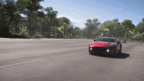 a red sports car is driving down a road with trees on the side of it
