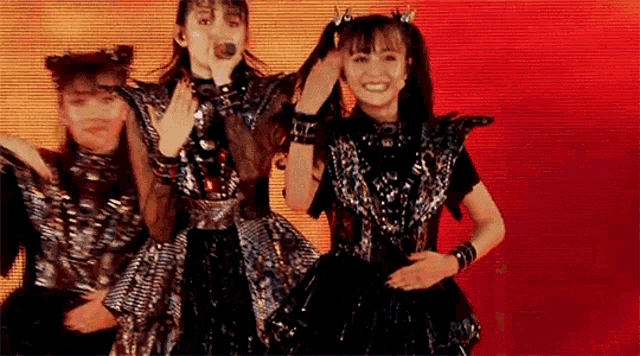 a group of girls are standing next to each other on a stage and singing into microphones .