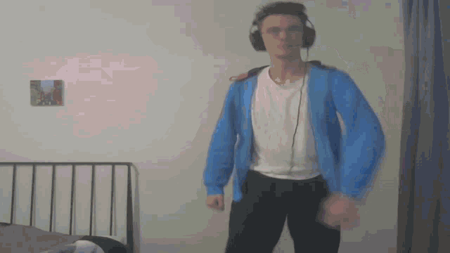 a man wearing headphones and a blue jacket is dancing in a bedroom