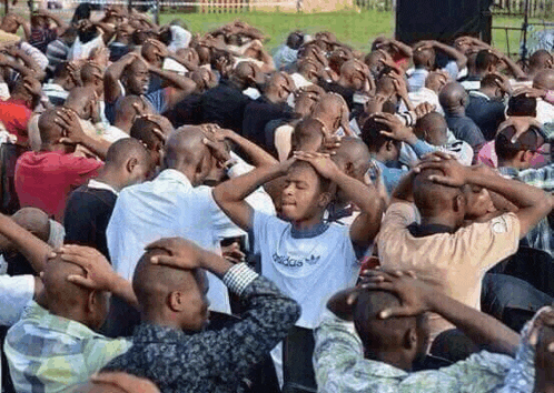 a group of men are sitting in a circle with their hands on their heads .