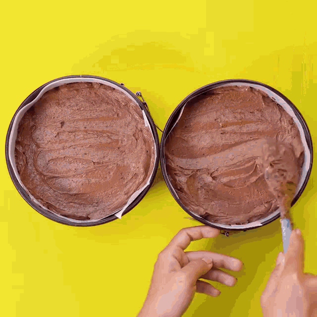 a person is spreading chocolate frosting in two pans with a spatula