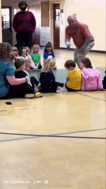a group of children are sitting on the floor watching a man do a trick