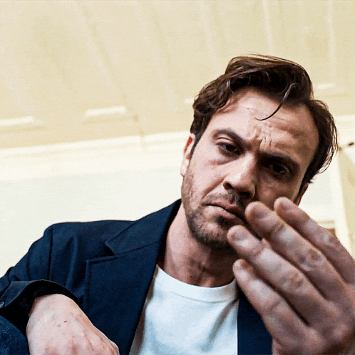 a man with a beard and a white shirt is holding his hand to his face