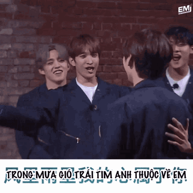 a group of young men are hugging each other in front of a brick wall with emi written in the corner
