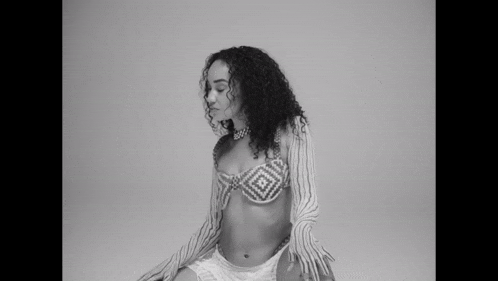 a black and white photo of a woman with curly hair wearing a bra and shorts .