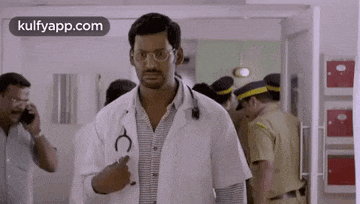 a man in a lab coat with a stethoscope around his neck is standing in a hallway .