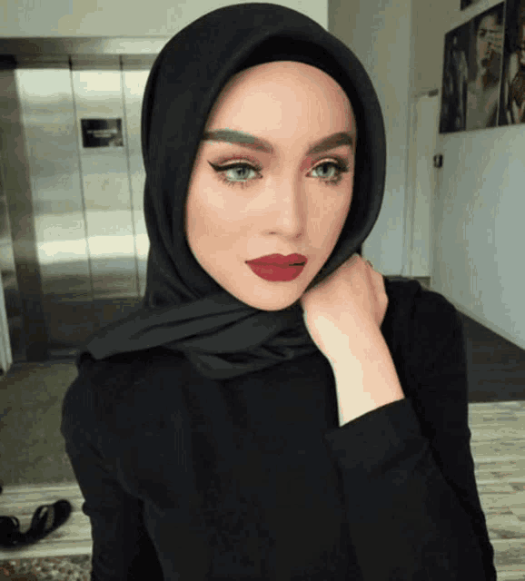 a woman wearing a black hijab with red lipstick looks at the camera