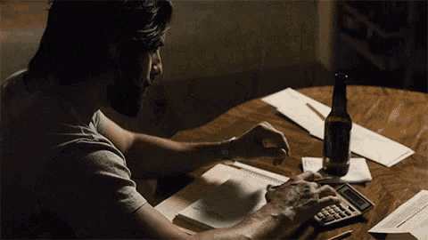 a man is using a calculator while sitting at a table with a bottle of beer