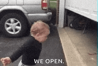 a baby is standing next to a car in a parking lot and saying `` we open '' .