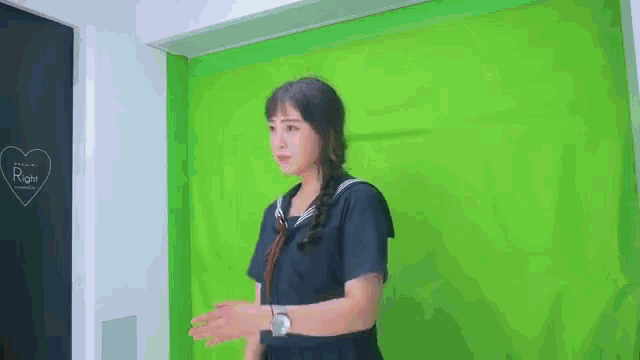 a woman in a black school uniform is standing in front of a green screen .