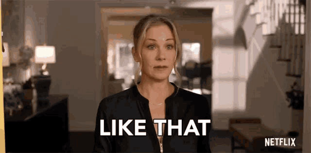 a woman is standing in a living room with the words `` like that '' behind her .