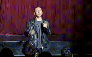 a man in a leather jacket is standing on a stage pointing