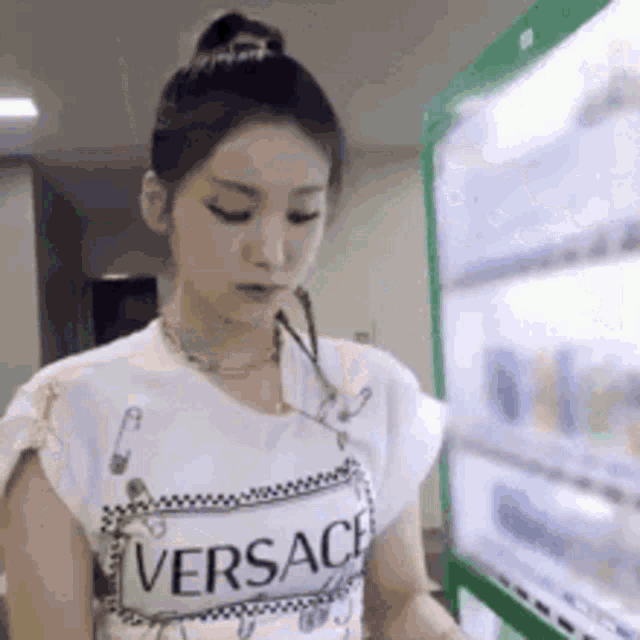 a woman is standing in front of a vending machine wearing a versace shirt .
