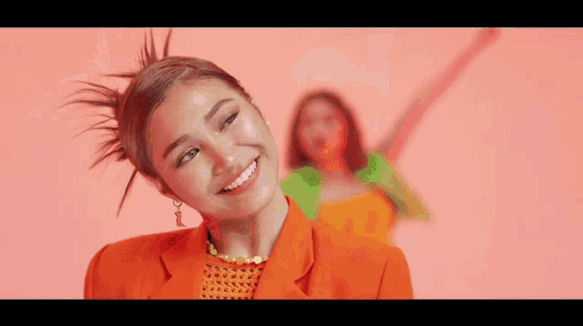 a woman in an orange jacket is smiling and holding a piece of paper in her hand .