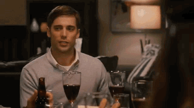 a man is sitting at a table with a bottle of beer and a glass of wine