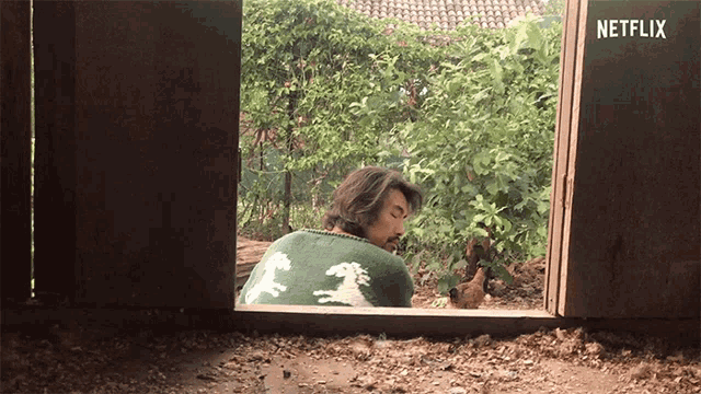 a man in a green and white sweater is looking out a window with netflix written on the wall behind him