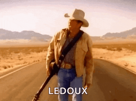 a man in a cowboy hat is walking down a road holding a guitar and says ledoux .
