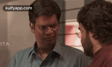 two men are standing next to each other and talking to each other . one of the men is wearing glasses .