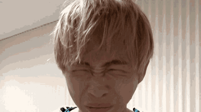 a person with blonde hair making a funny face with their eyes closed