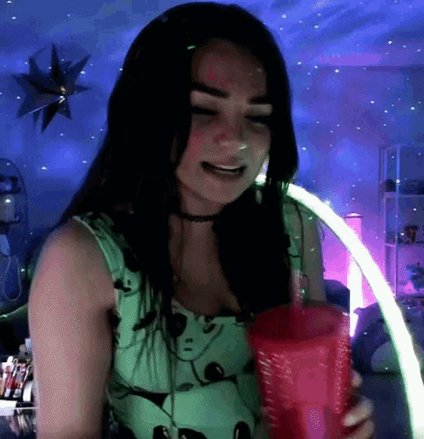 a woman is holding a pink cup with a straw in her hand in front of a starry night sky .