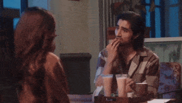 a man and a woman are sitting at a table with drinks and talking to each other .