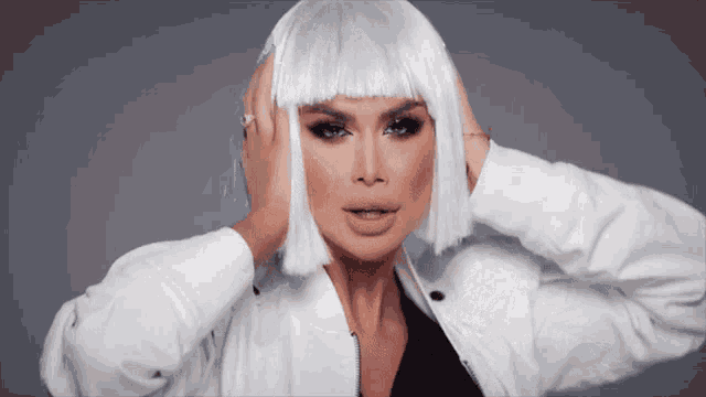 a woman wearing a white wig holds her hand to her head