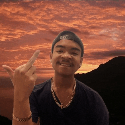 a young man wearing a hat and a necklace giving the middle finger