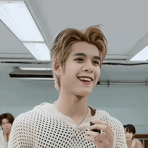 a young man in a white sweater is smiling in a room