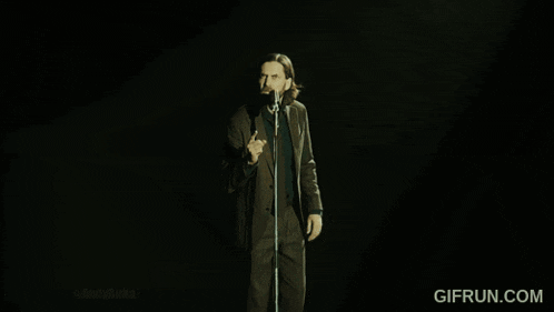 a man in a suit and tie is singing into a microphone with gifrun.com in the corner