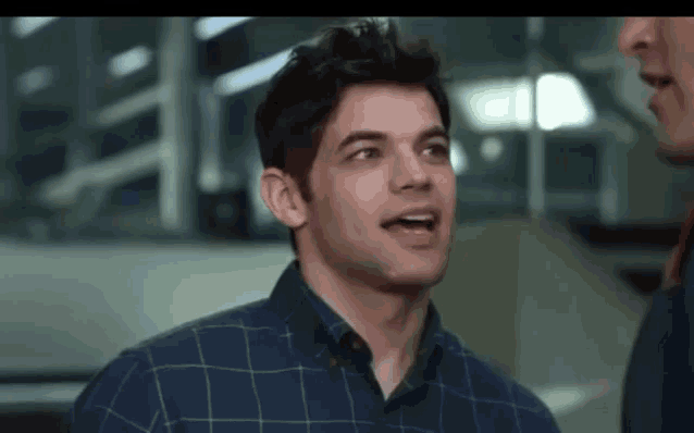 a man in a plaid shirt is talking to another man in a room .