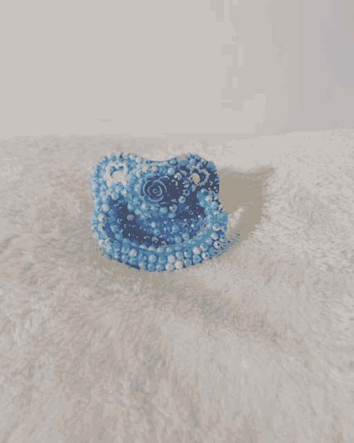a blue pacifier with pearls and a rose sits on a white blanket