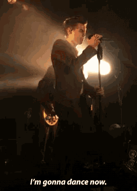 a man singing into a microphone with the words " i 'm gonna dance now " underneath him