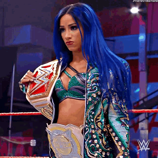 a woman with blue hair is standing in a wrestling ring holding a world heavyweight championship belt .