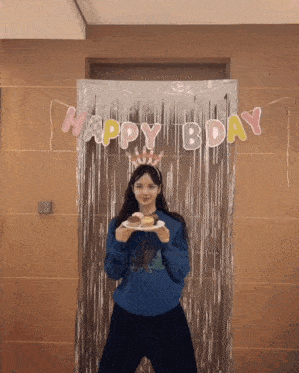 a woman holding a plate of food in front of a happy bday banner