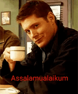 a man sitting at a table holding a cup of coffee with the words assalamualaikum on the bottom right