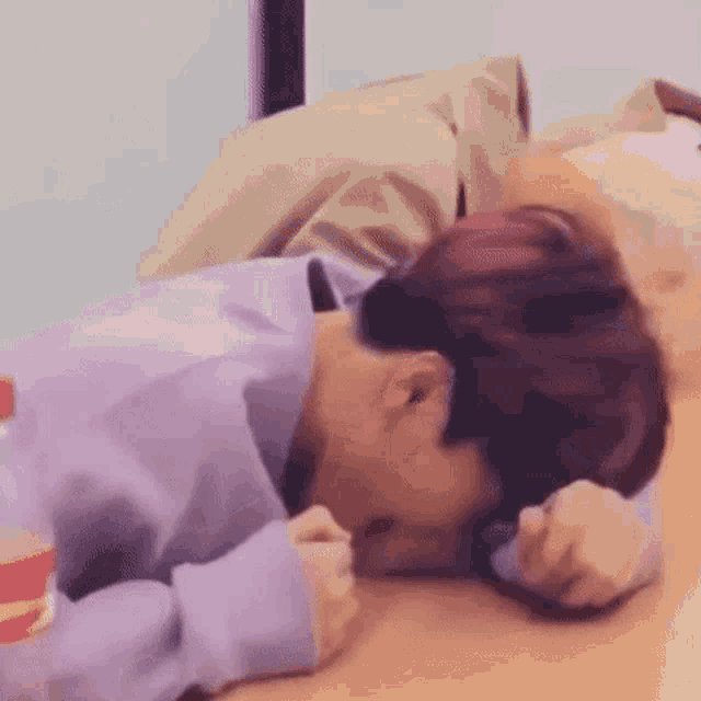 a man in a purple sweater is laying on a wooden table with his head on a pillow .