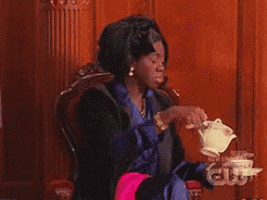 a woman is sitting in a chair pouring a cup of tea from a teapot .