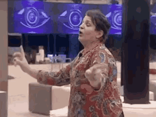 a woman in a floral shirt is standing in front of a large screen .
