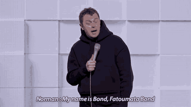 a man in a black hoodie is holding a microphone and saying norman my name is bond fatoumata bond