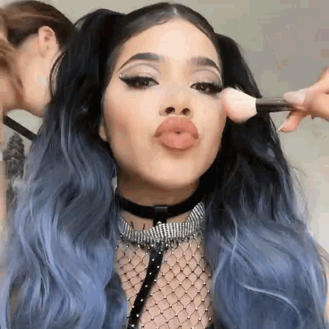 a woman with blue hair is getting her makeup applied by another woman