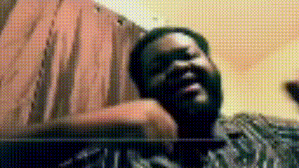 a man with a beard is sitting in front of a curtain and looking at the camera .